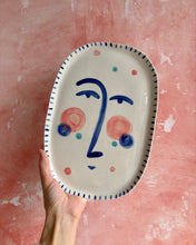 Carica l'immagine nel visualizzatore di Gallery, Oval ceramic plate with artistic face design held against a pink background