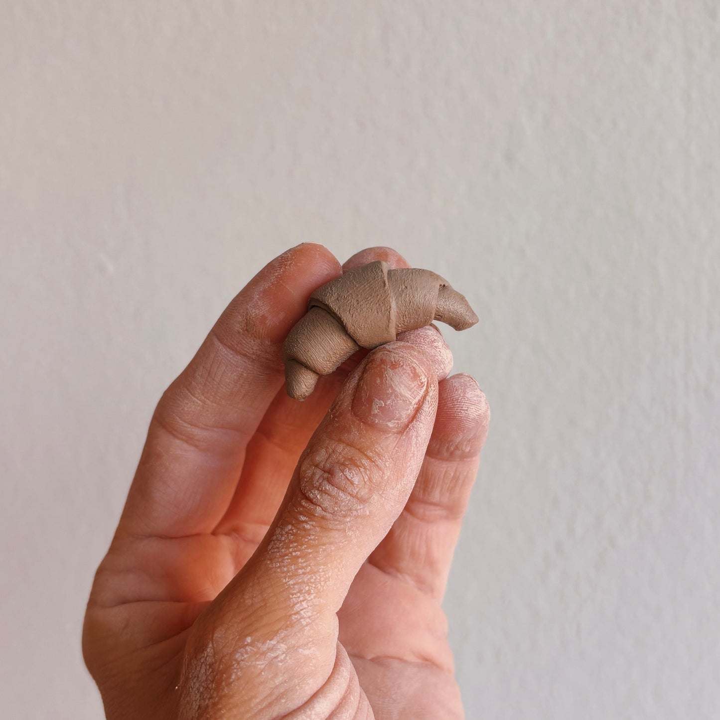 Hand holding a small clay croissant sculpture, demonstrating craftsmanship and creativity.