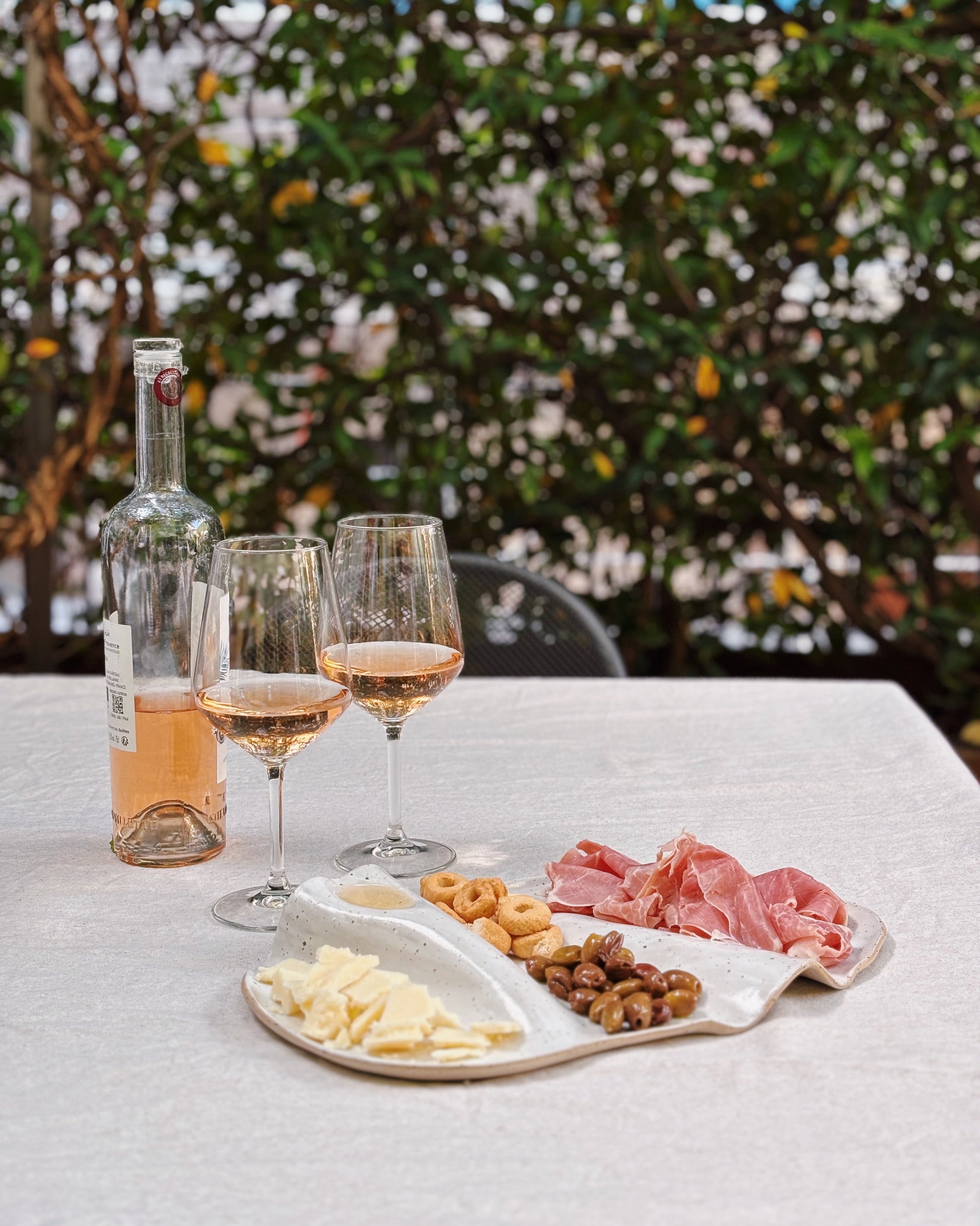 Wine glasses with pink wine, a bottle of wine, and a charcuterie board on a table outdoors.