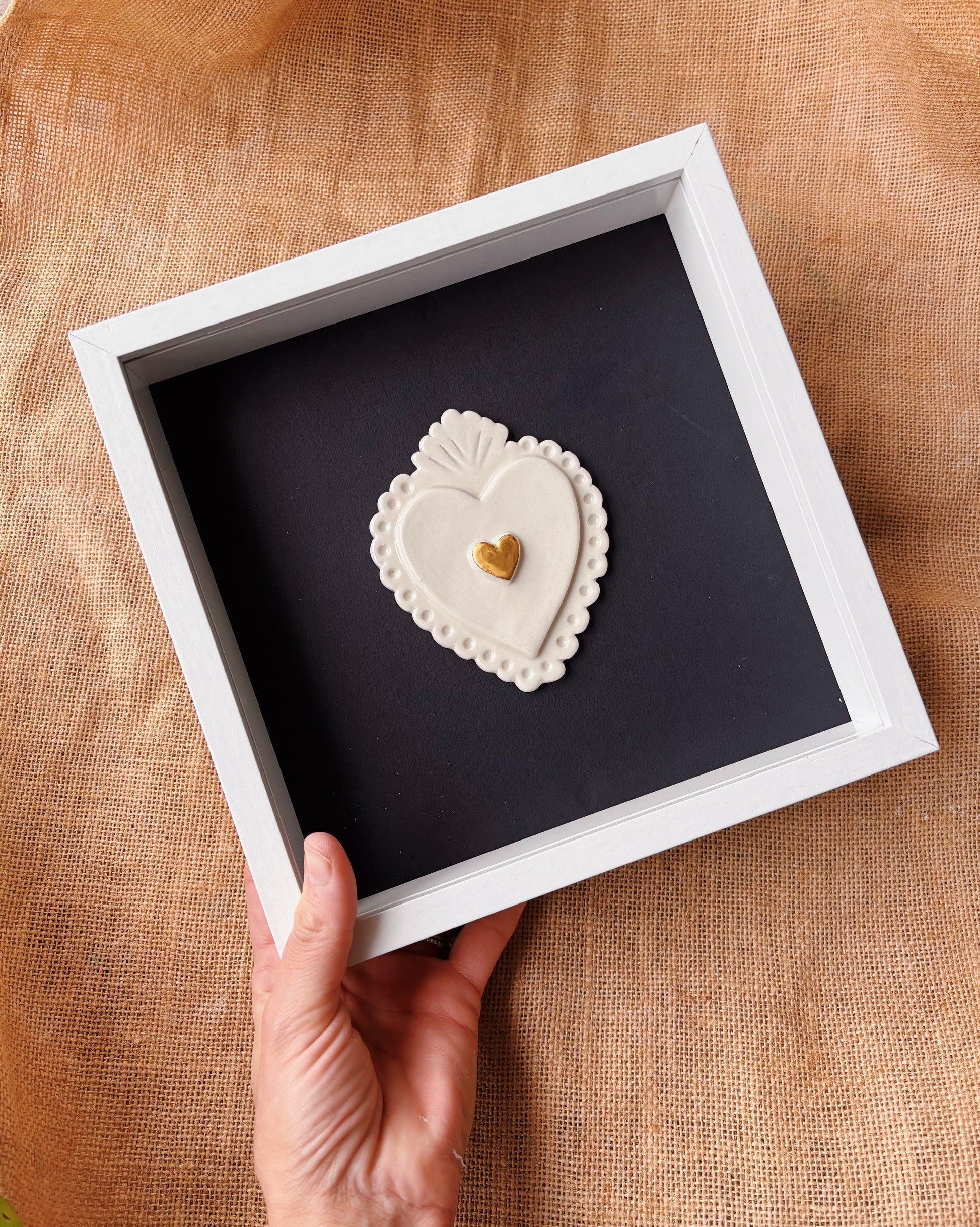 Heart-shaped decorative item in a white frame held by a hand on a textured surface
