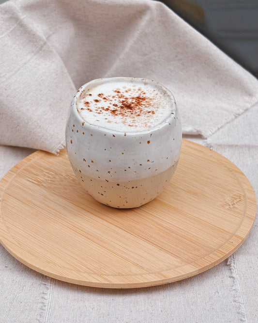 Cup of coffee with whipped cream and cinnamon on a wooden coaster with a beige cloth background