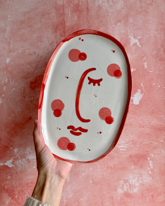 Ceramic plate with a face design held against a pink background

