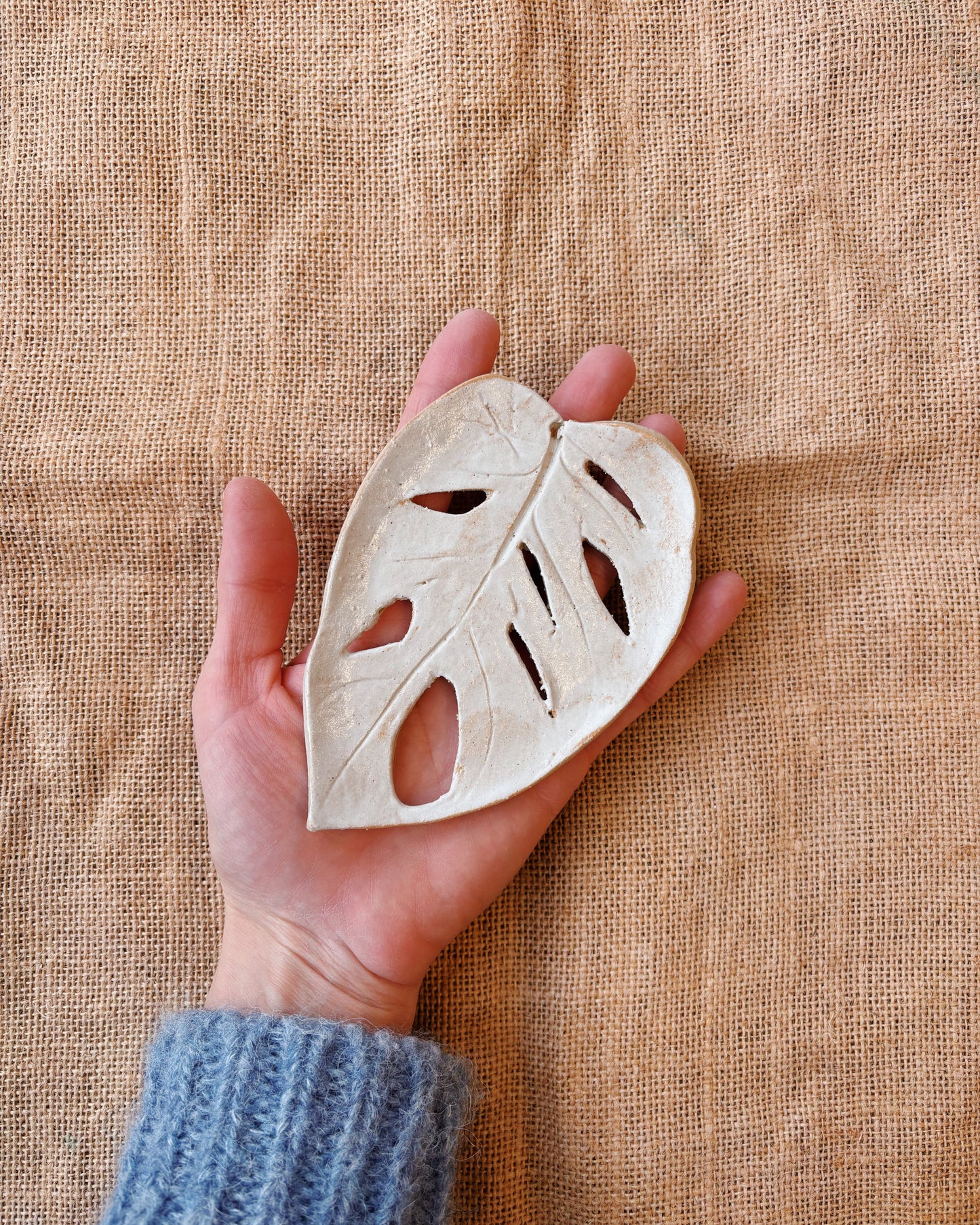 Hand holding a ceramic leaf-shaped ornament against a textured beige background