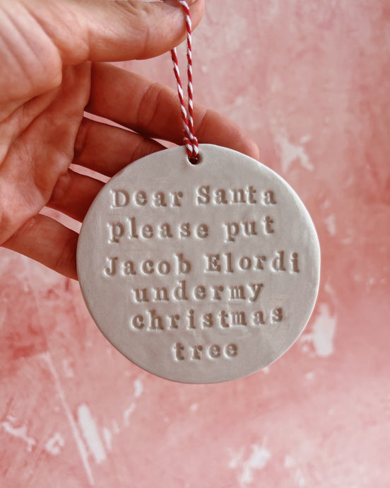 A hand holding a Christmas decoration on a pink background