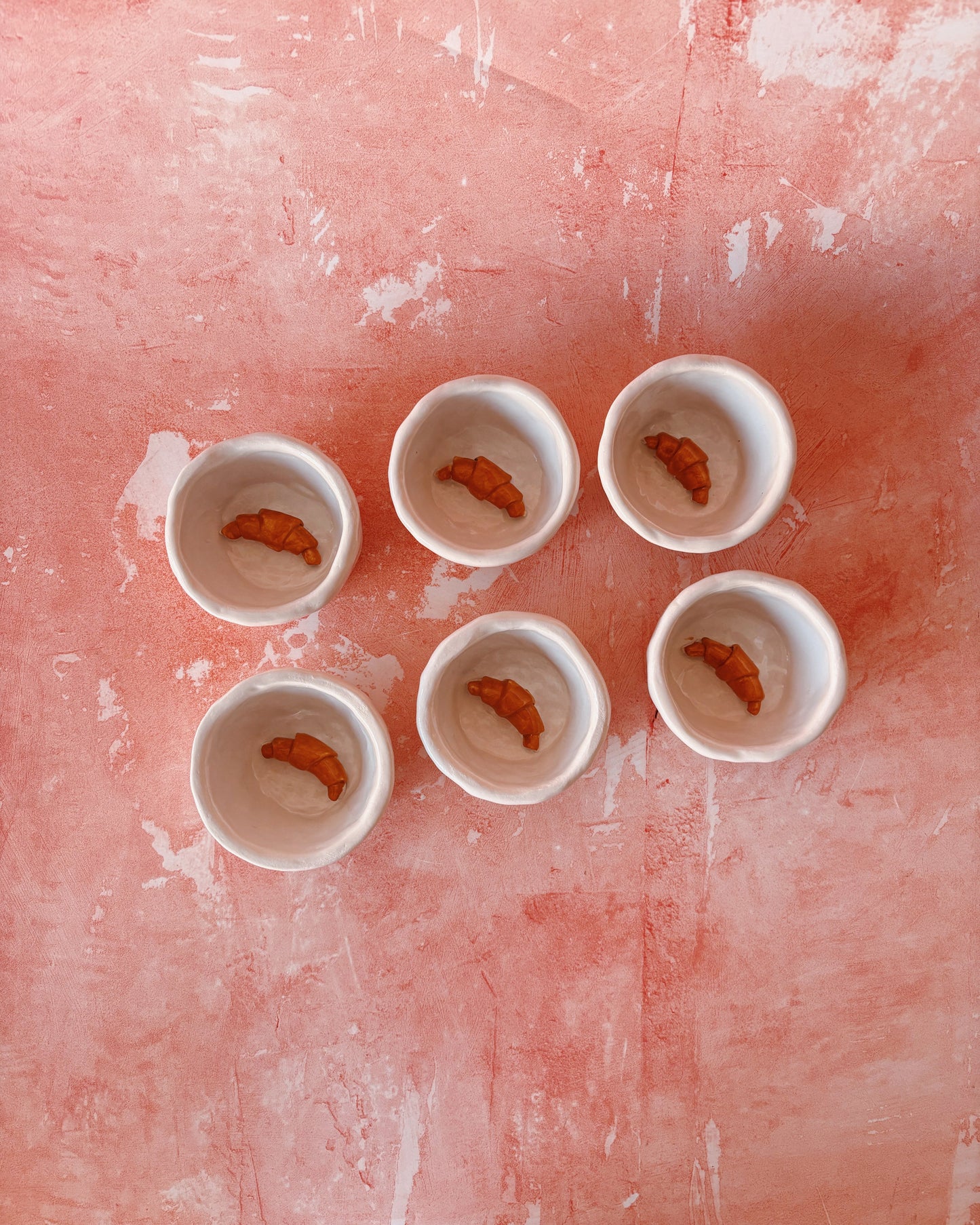 Croissant Espresso Mugs - Set of 6 arranged on a textured pink surface with croissant design inside each mug.