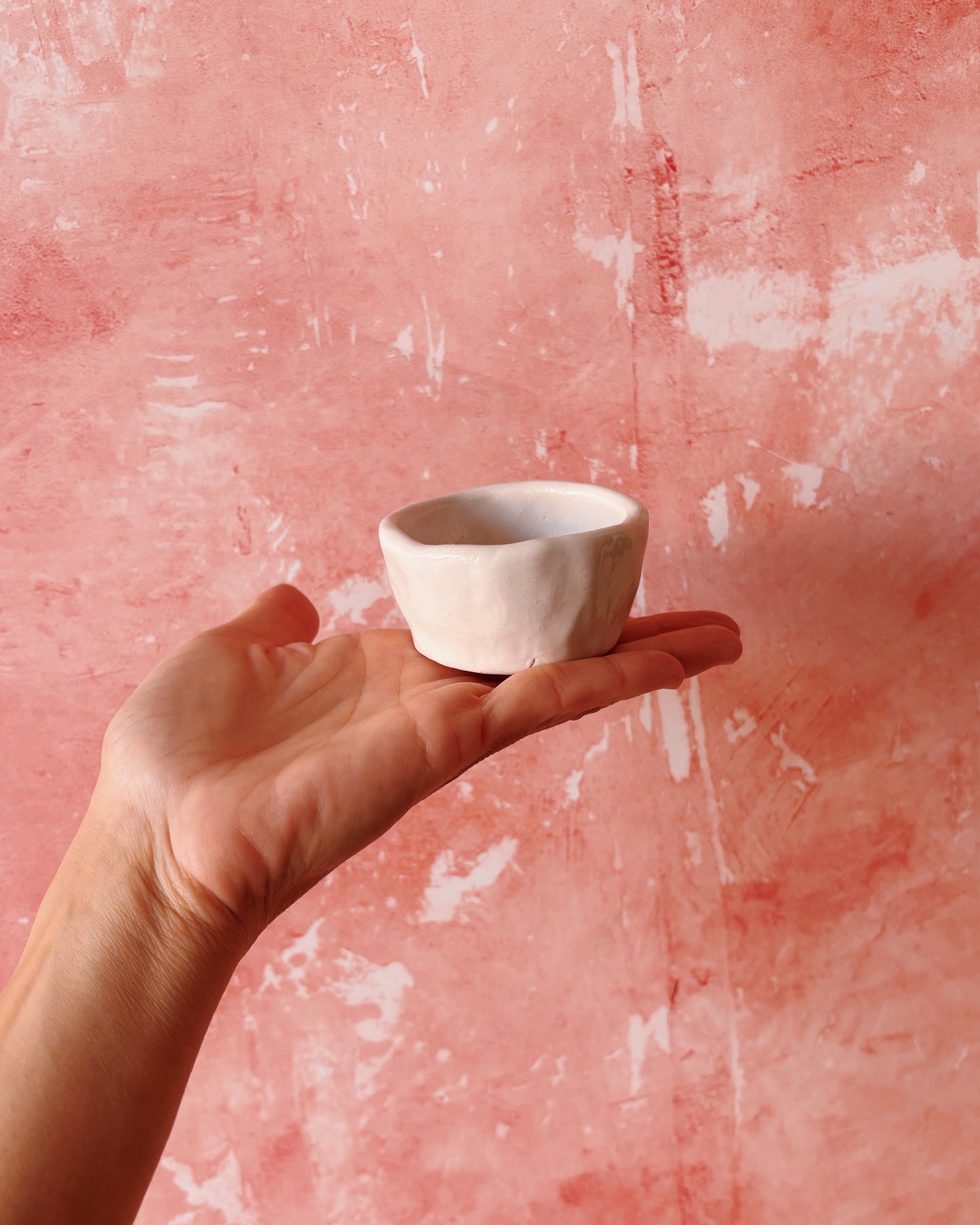 Hand holding a handmade stoneware mug against a pink textured background, showcasing a Croissant Espresso Mug - Set of 6.