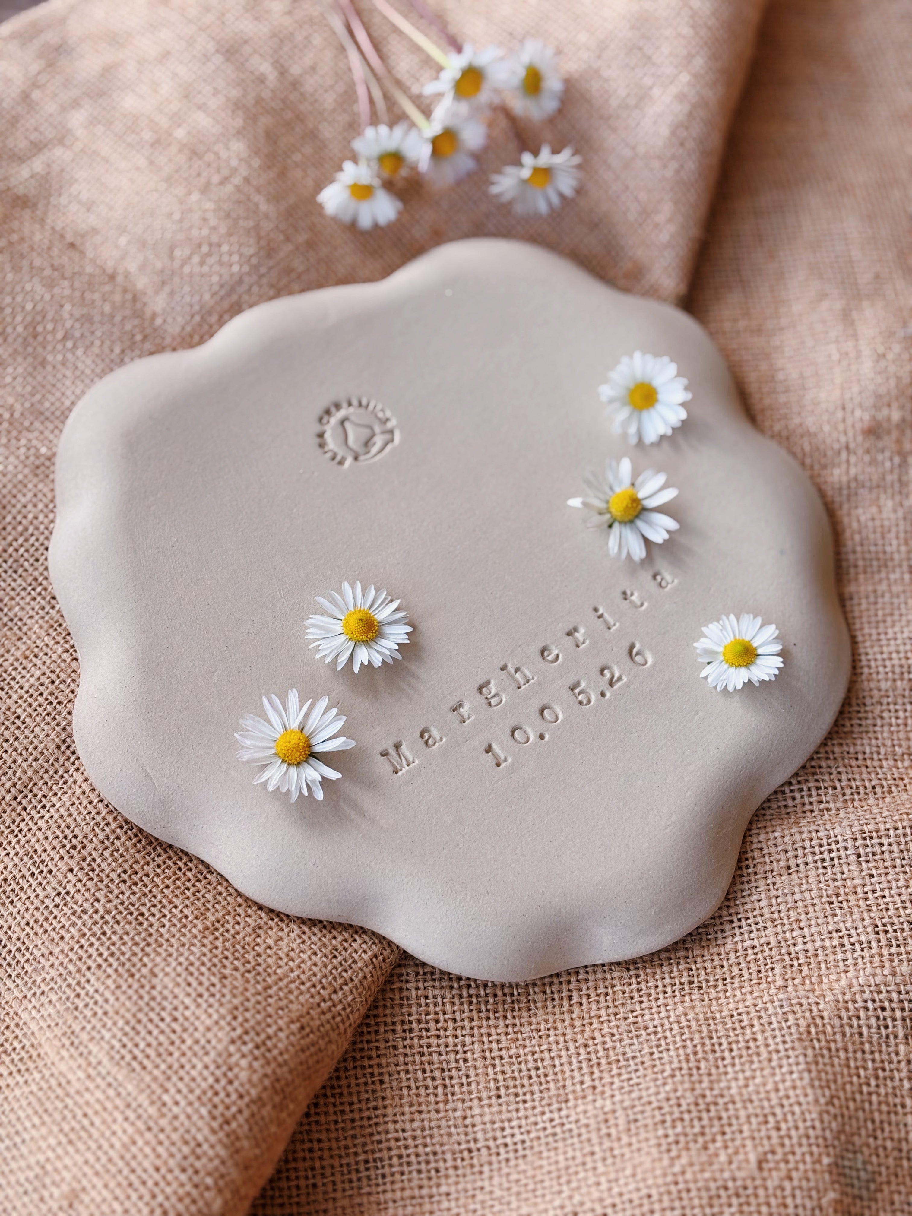 Ceramic plate with daisies and engraved text on a textured fabric background