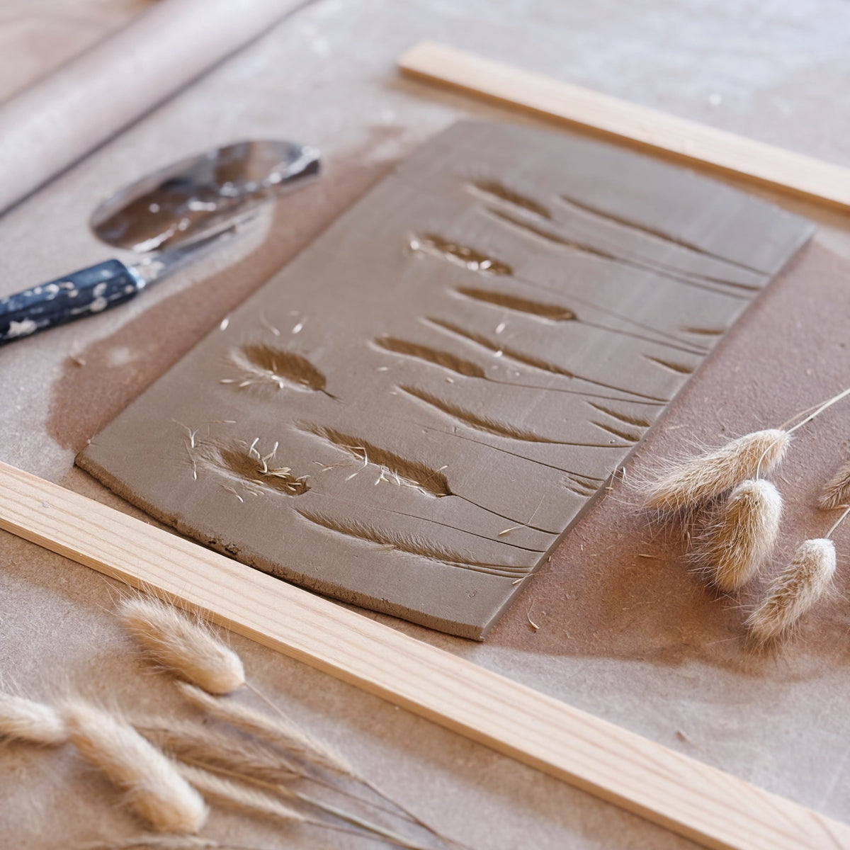 Clay slab with textured patterns and wooden tools on a table