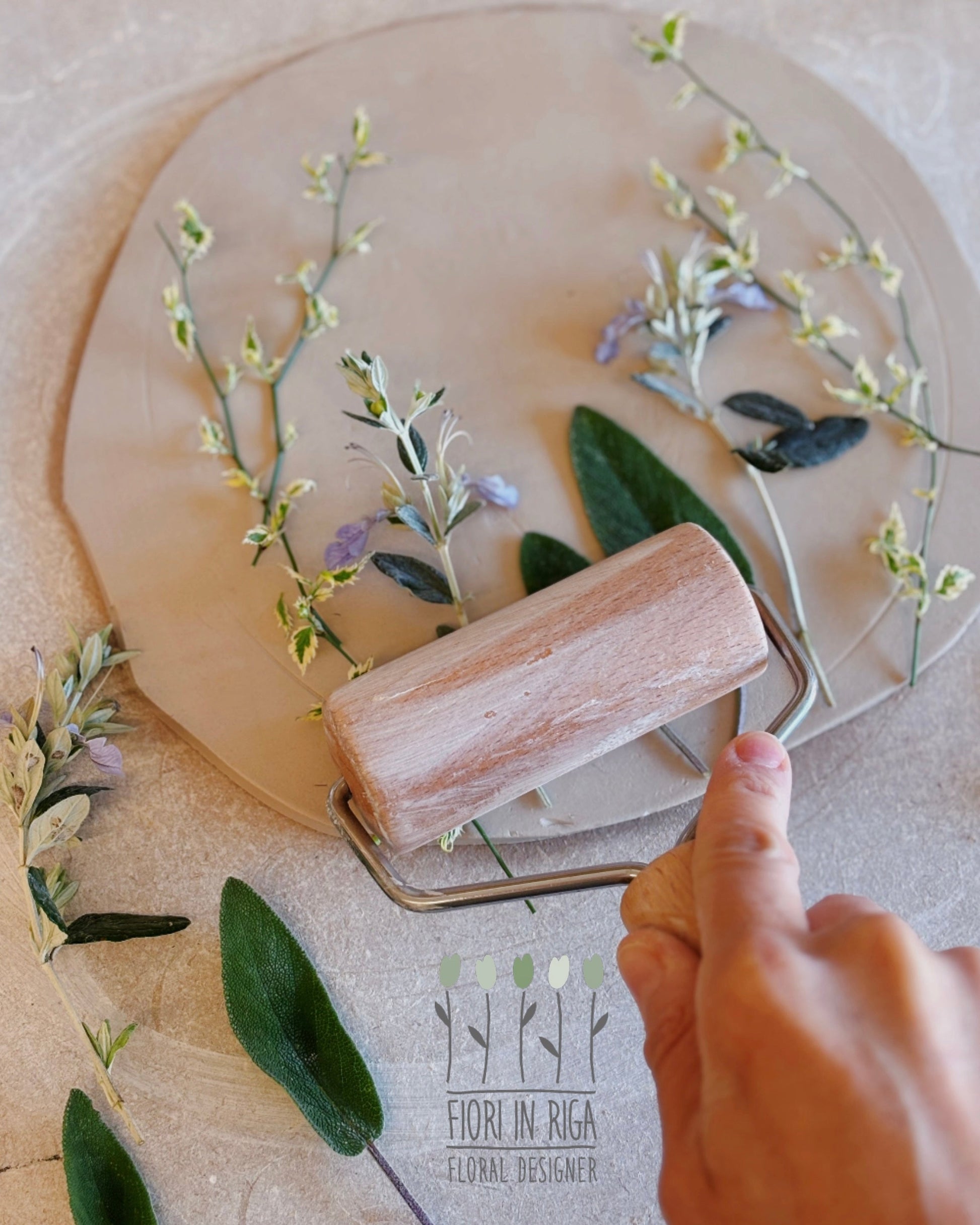 Person using a wooden roller on a surface with floral elements and a visible brand name.