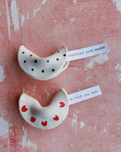 Load image into Gallery viewer, Two ceramic fortune cookies with polka dots and hearts on a textured pink surface.
