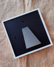 Load image into Gallery viewer, Backside of a picture frame with a black mat and silver metal piece on a wooden surface.
