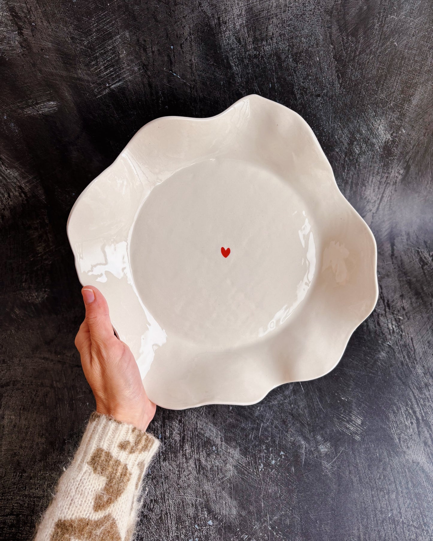 A hand holding a ceramic bowl with a tiny heart in the middle on a black background