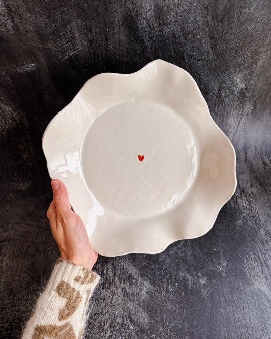 A hand holding a ceramic bowl with a tiny heart in the middle on a black background