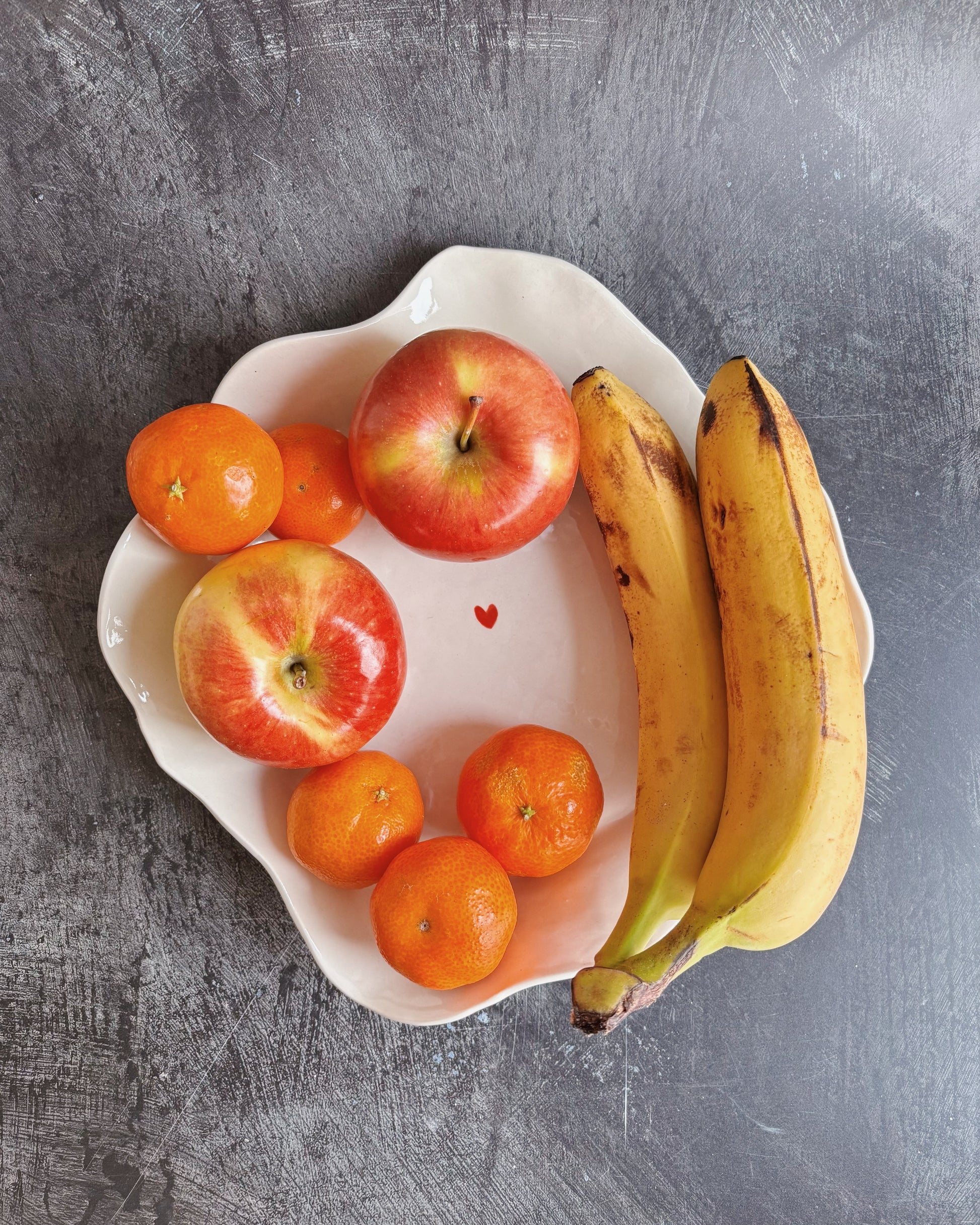 A ceramic bowl with fruits in it and a tiny heart in the middle on a black background
