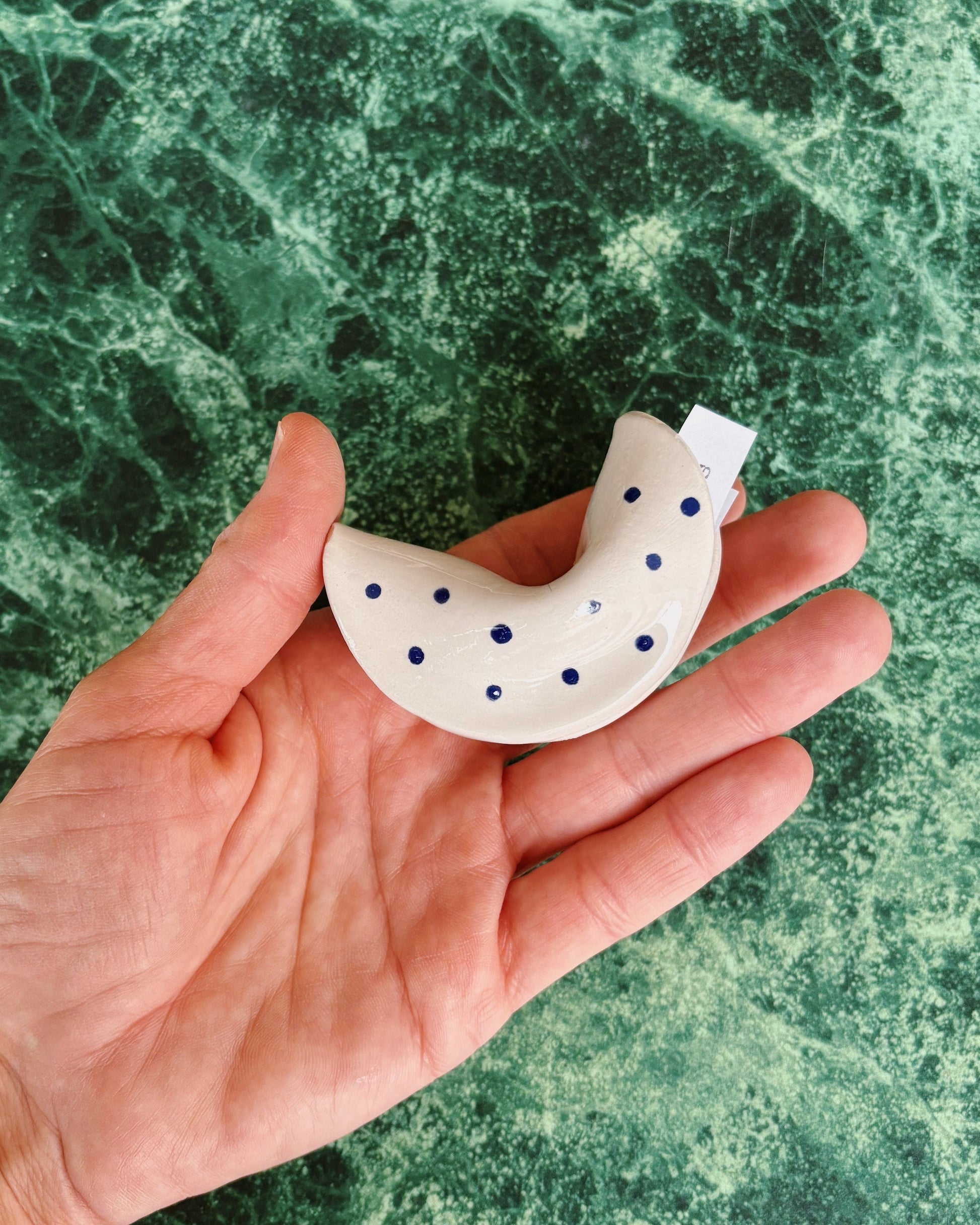 Hand holding a white ceramic fortune cookie with blue dots against a green marble background