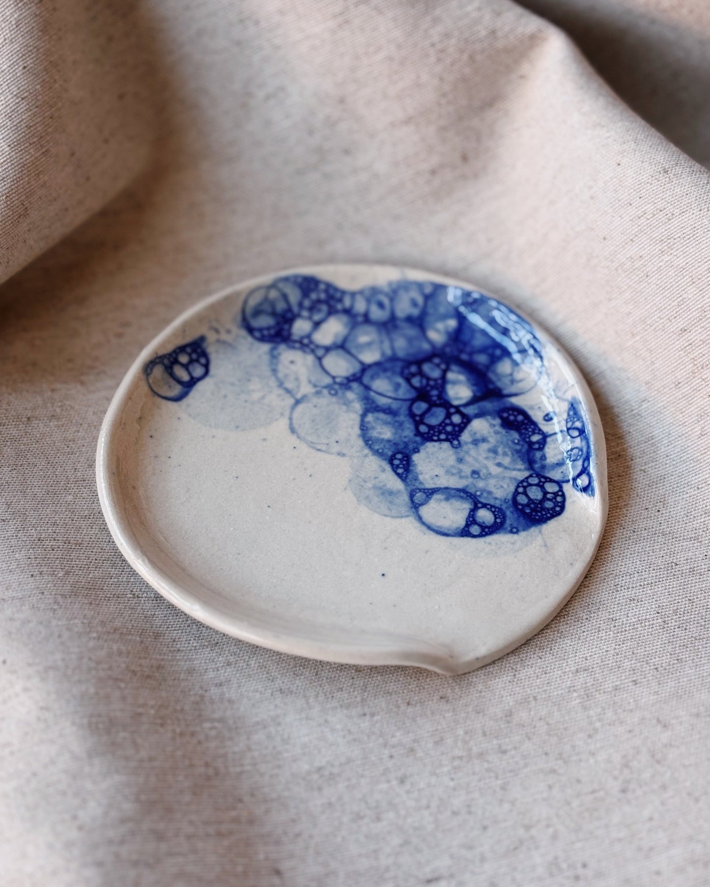 Small ceramic plate with blue abstract design on a beige fabric background