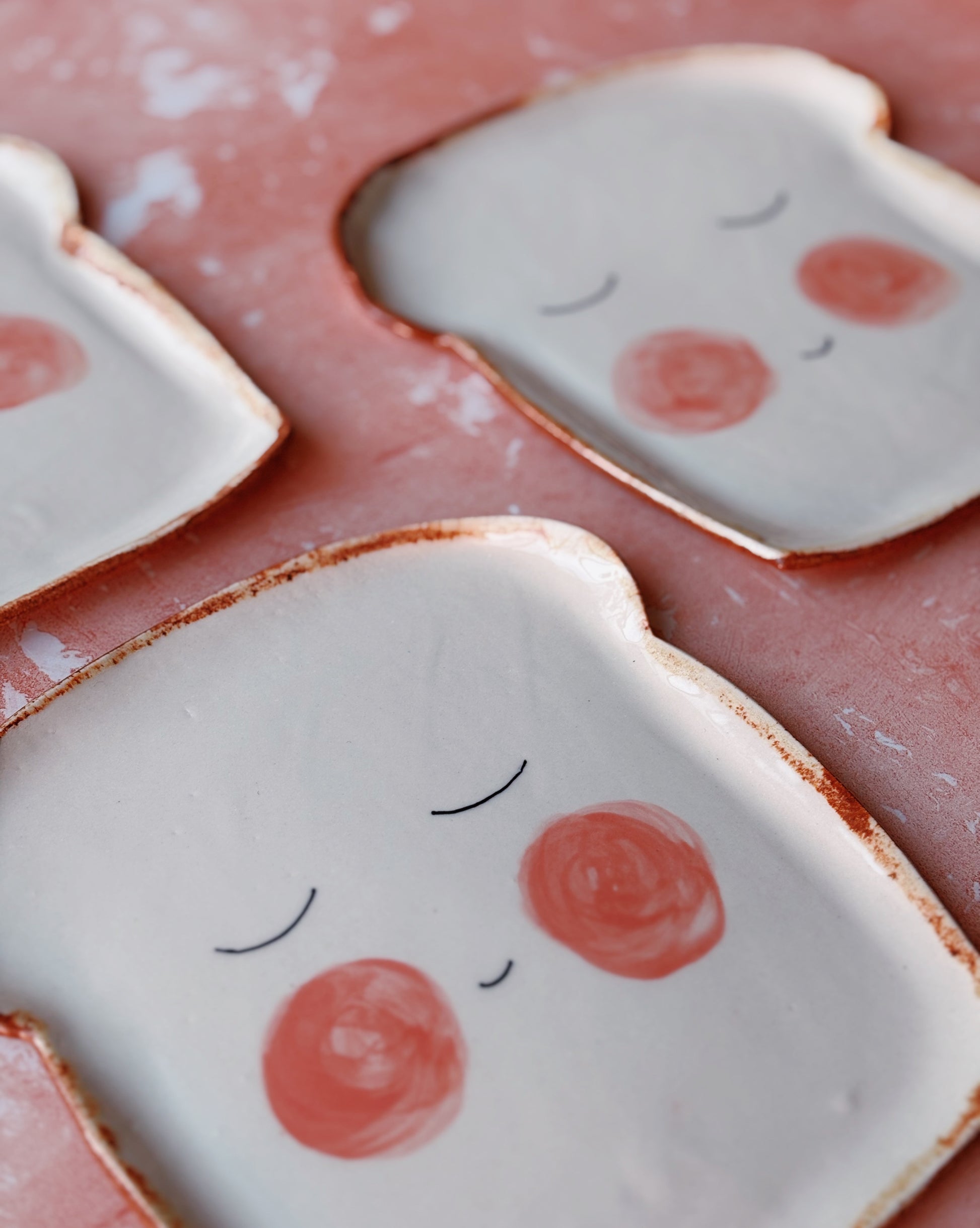 Ceramic bread-shaped plates with red cheeks on a pink background