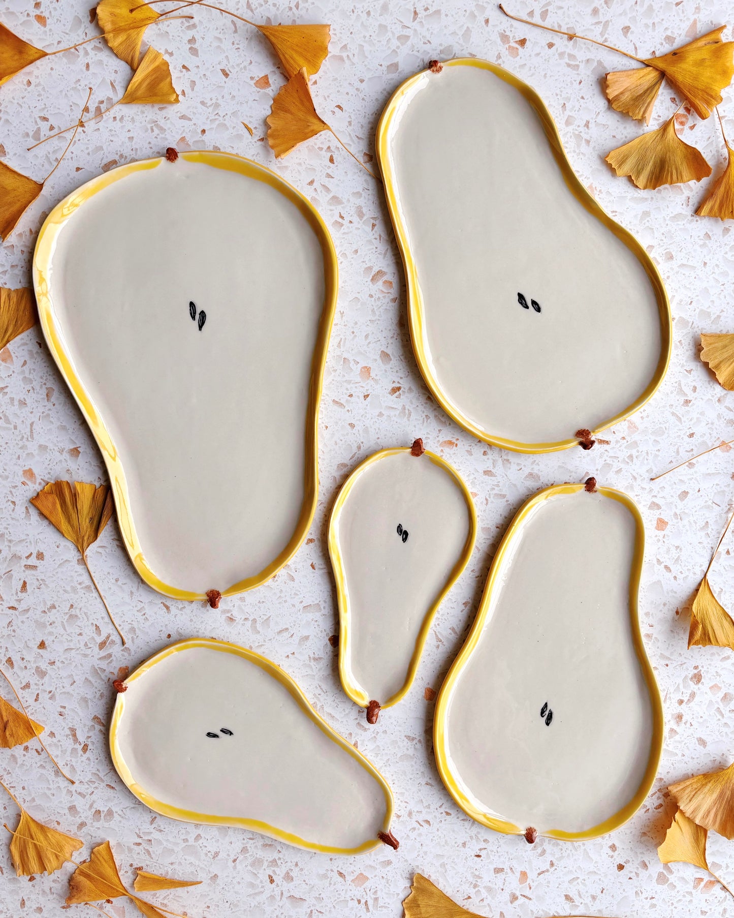 Ceramic pear-shaped plates with gold edges on a textured surface with dried leaves.