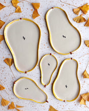 Load image into Gallery viewer, Ceramic pear-shaped plates with gold edges on a textured surface with dried leaves.
