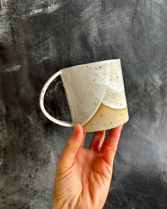 A hand holding a mug with a special speckled effect clay on a black background