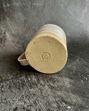 Carica l'immagine nel visualizzatore di Gallery, Bottom of a mug branded with a special speckled clay on a black background
