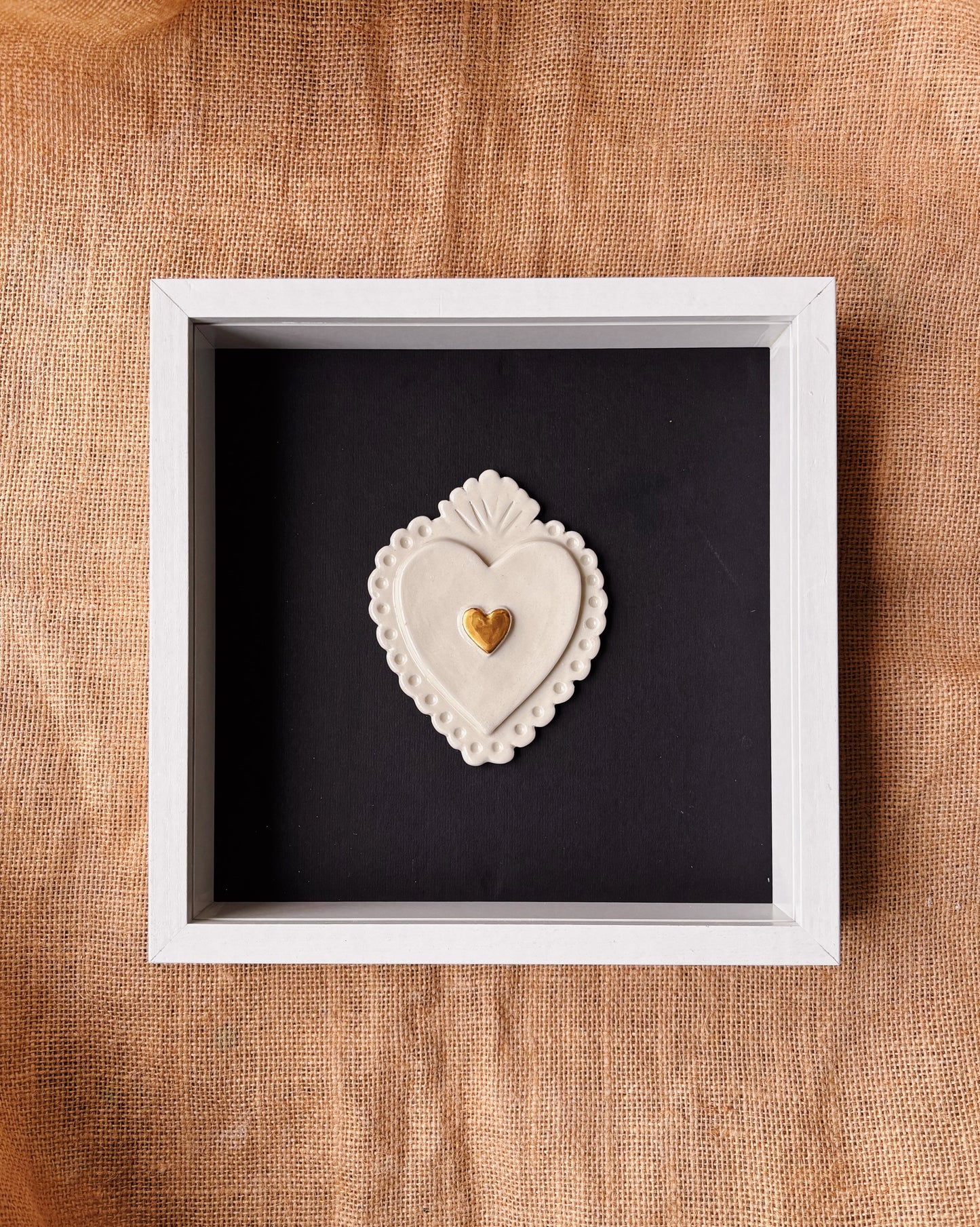 Decorative heart-shaped object in a white frame on a textured brown surface