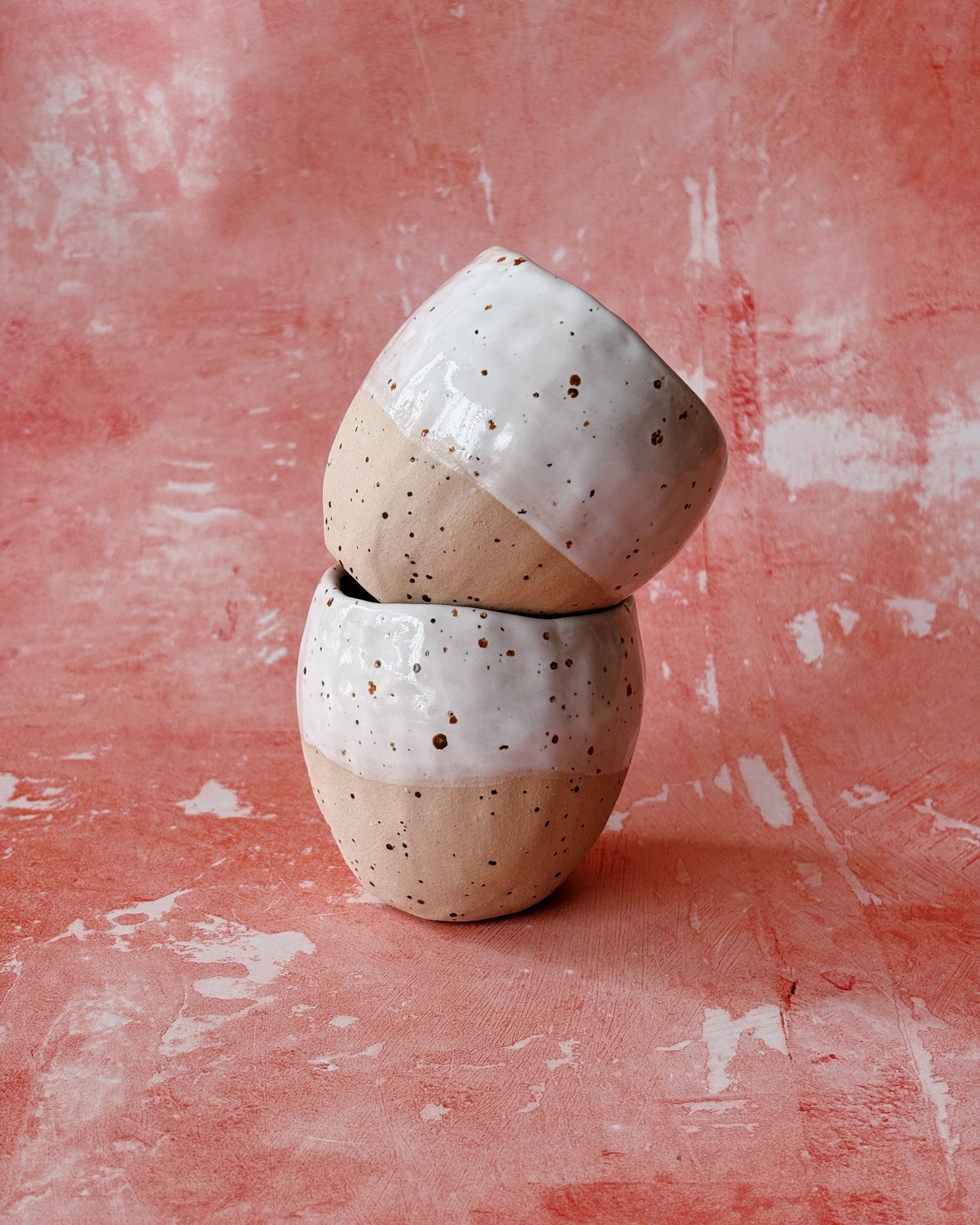 Two ceramic cups stacked on a textured pink surface