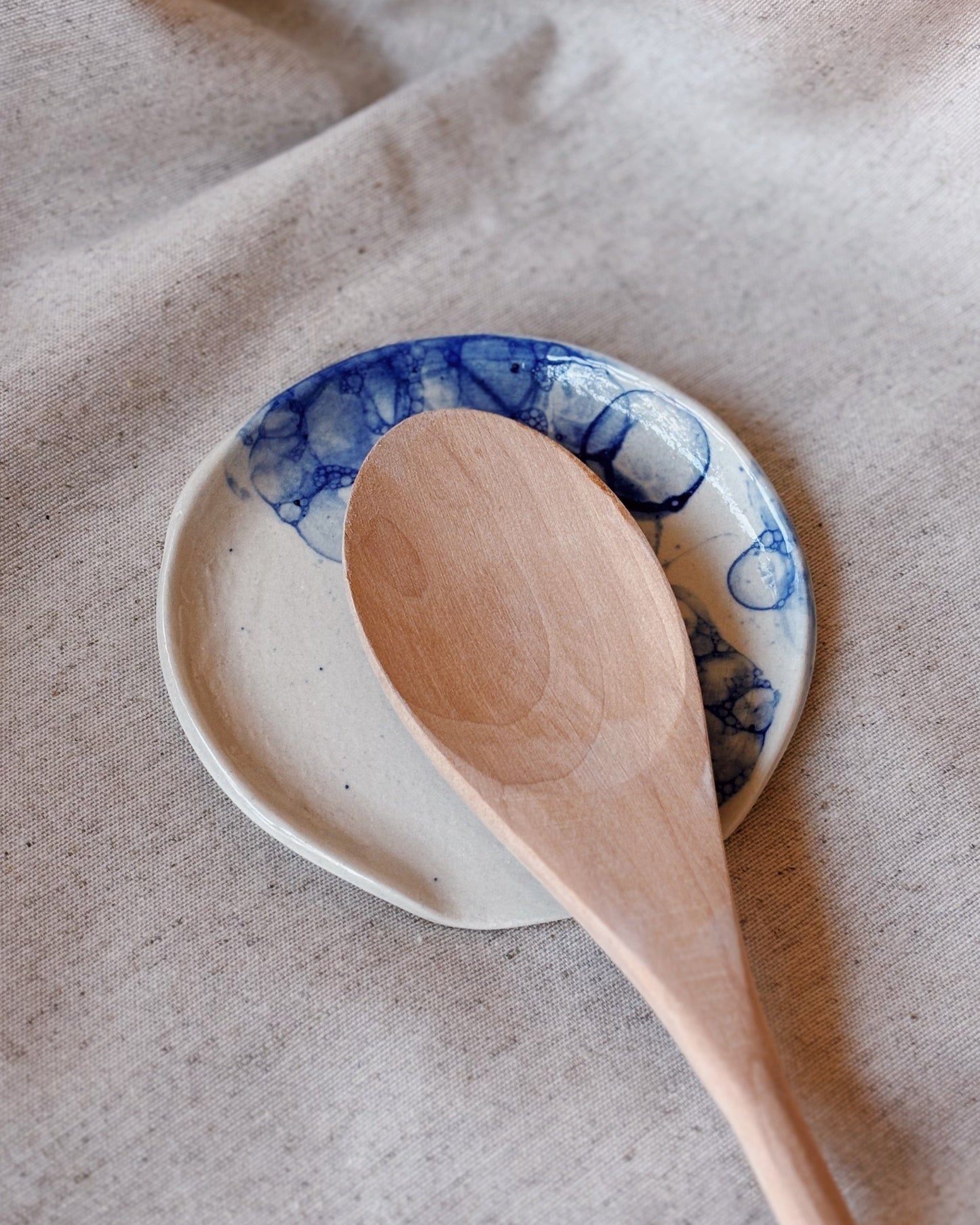 A ceramic white spoon rest with a marble blue effect and a wooden spoon lying on top of it