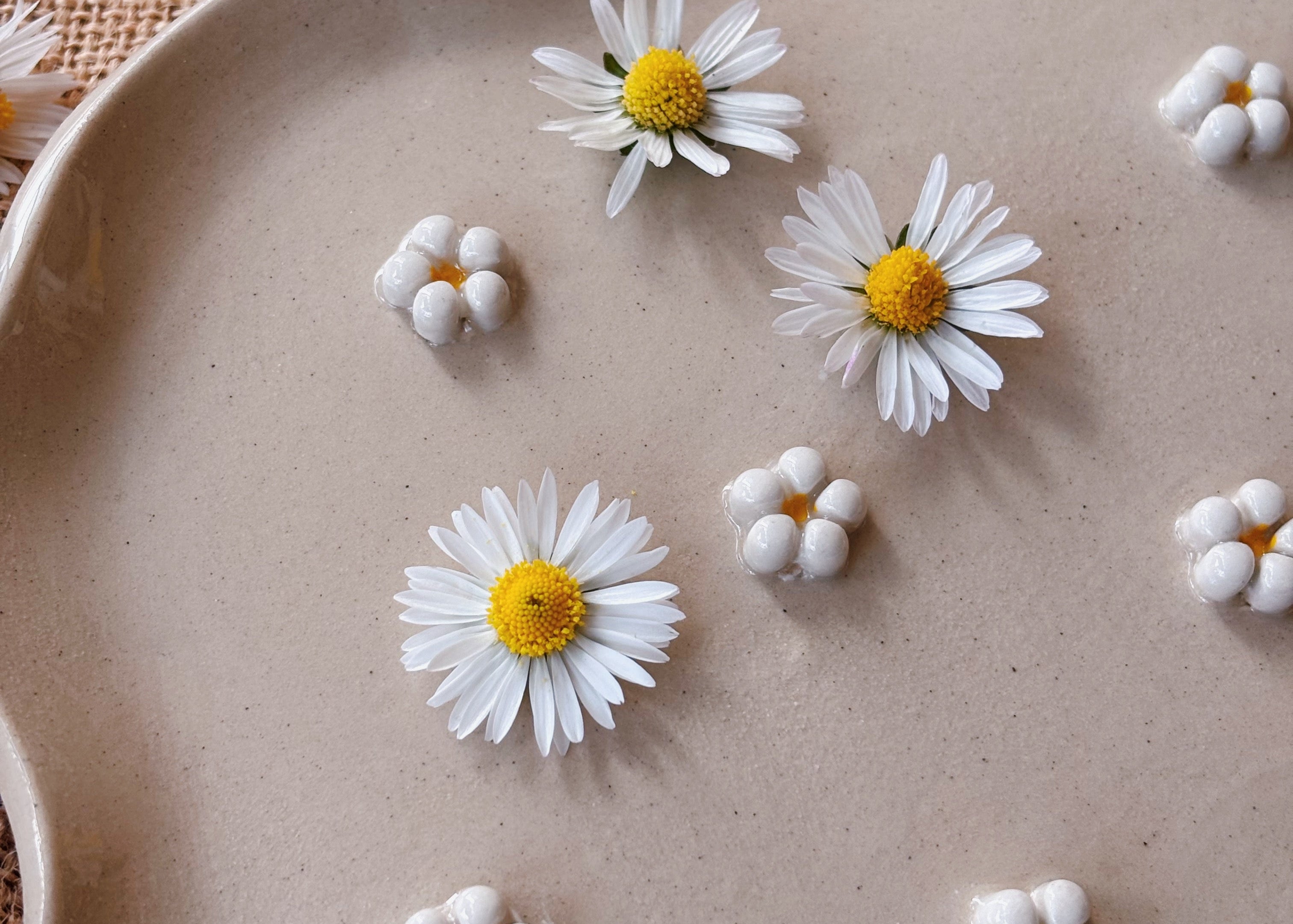 White flowers with yellow centers on a beige plate against a woven background