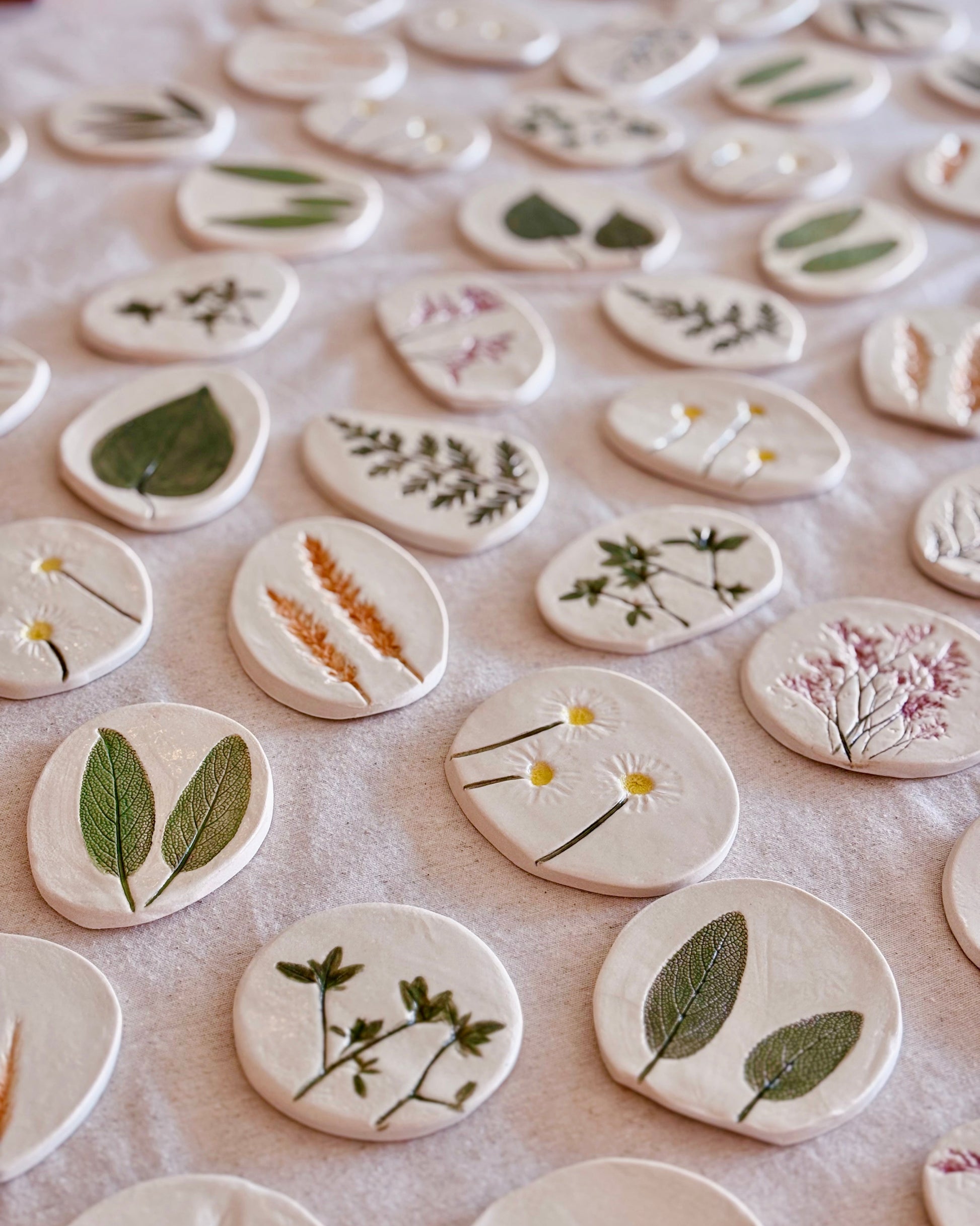 Collection of small ceramic tiles with plant designs on a white surface