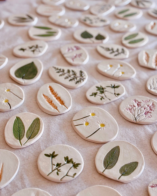 Collection of small ceramic tiles with plant designs on a white surface
