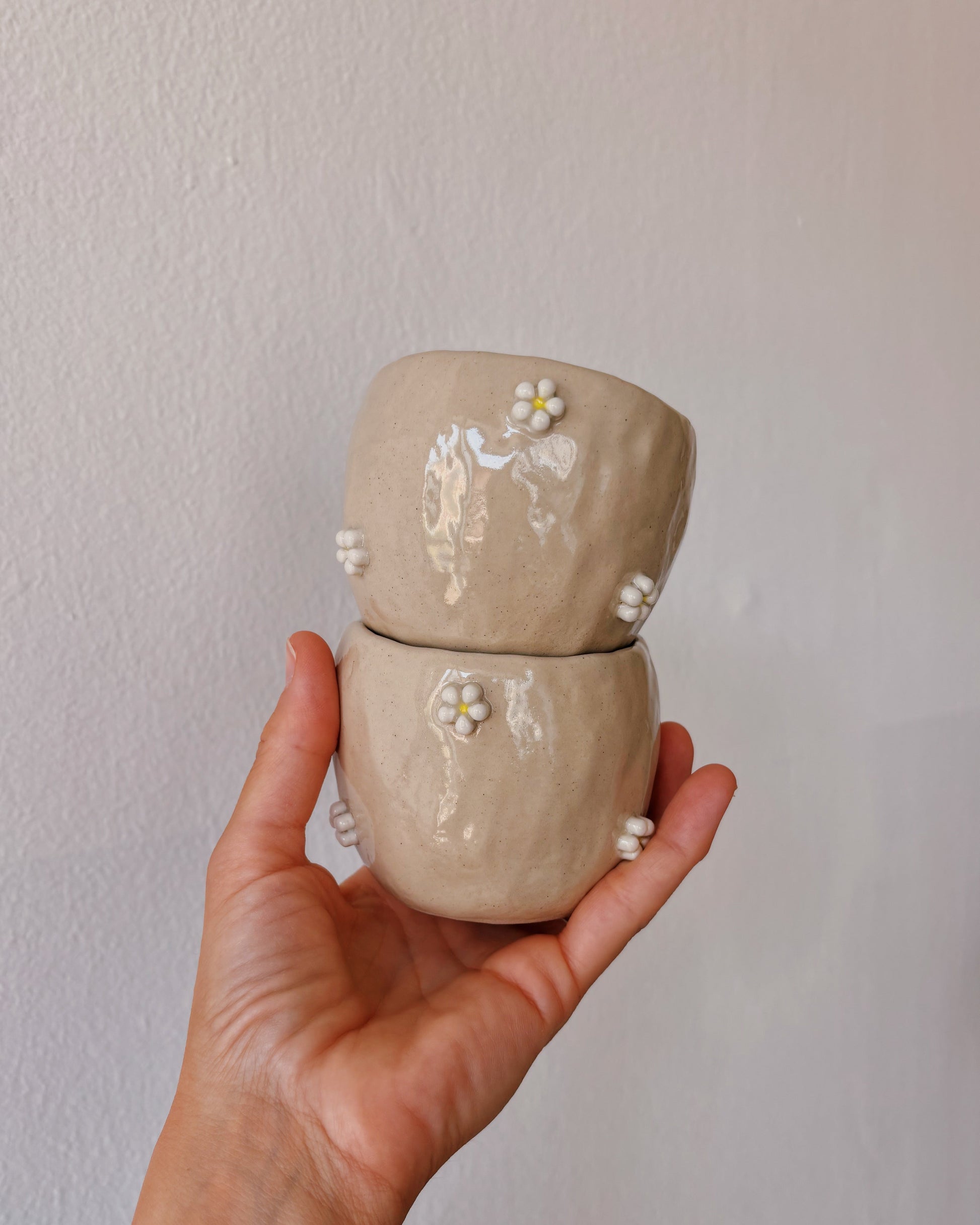 Hand holding a small ceramic jar with floral designs against a plain background