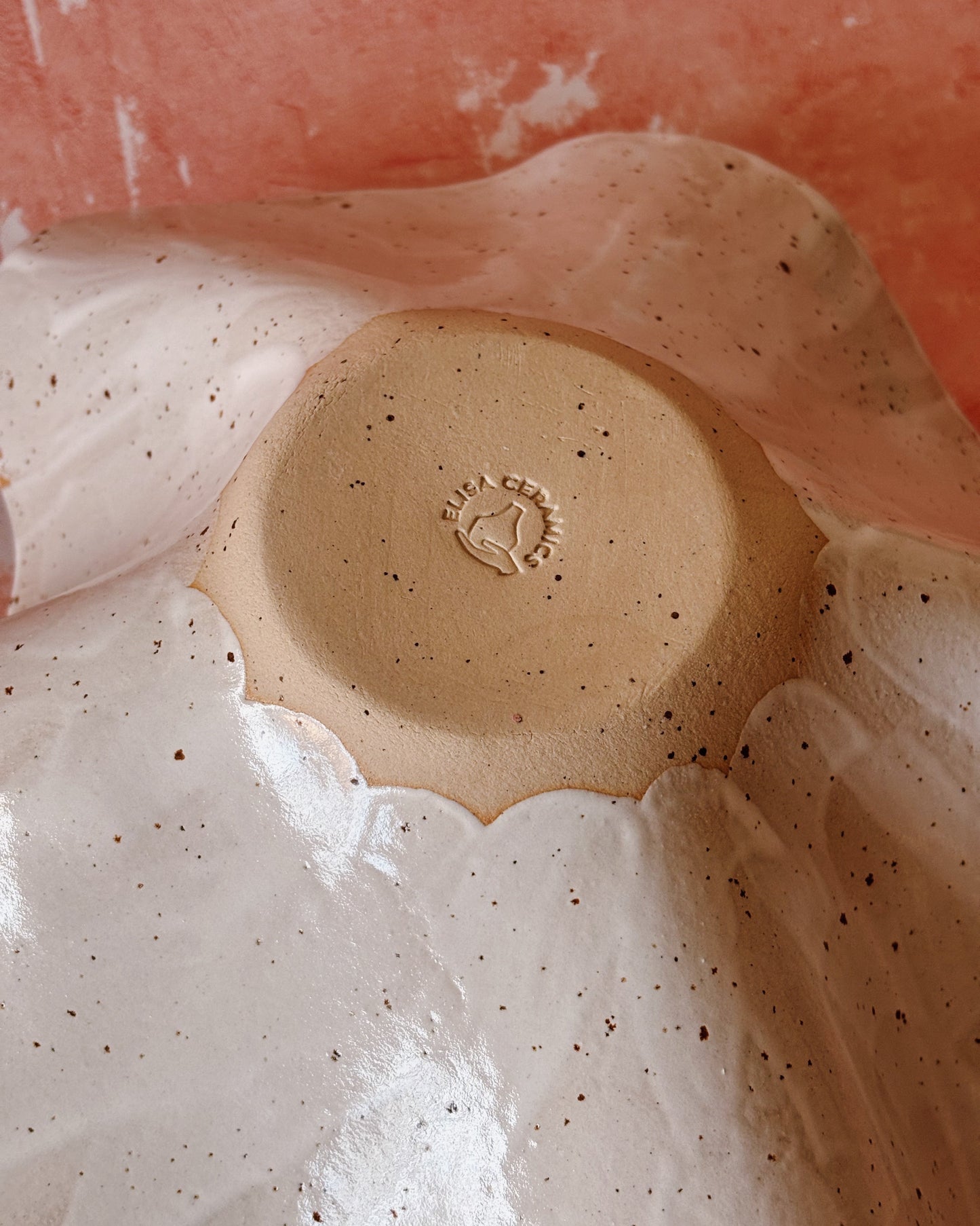 Close-up of a ceramic plate with speckled glaze and a logo on a pink background