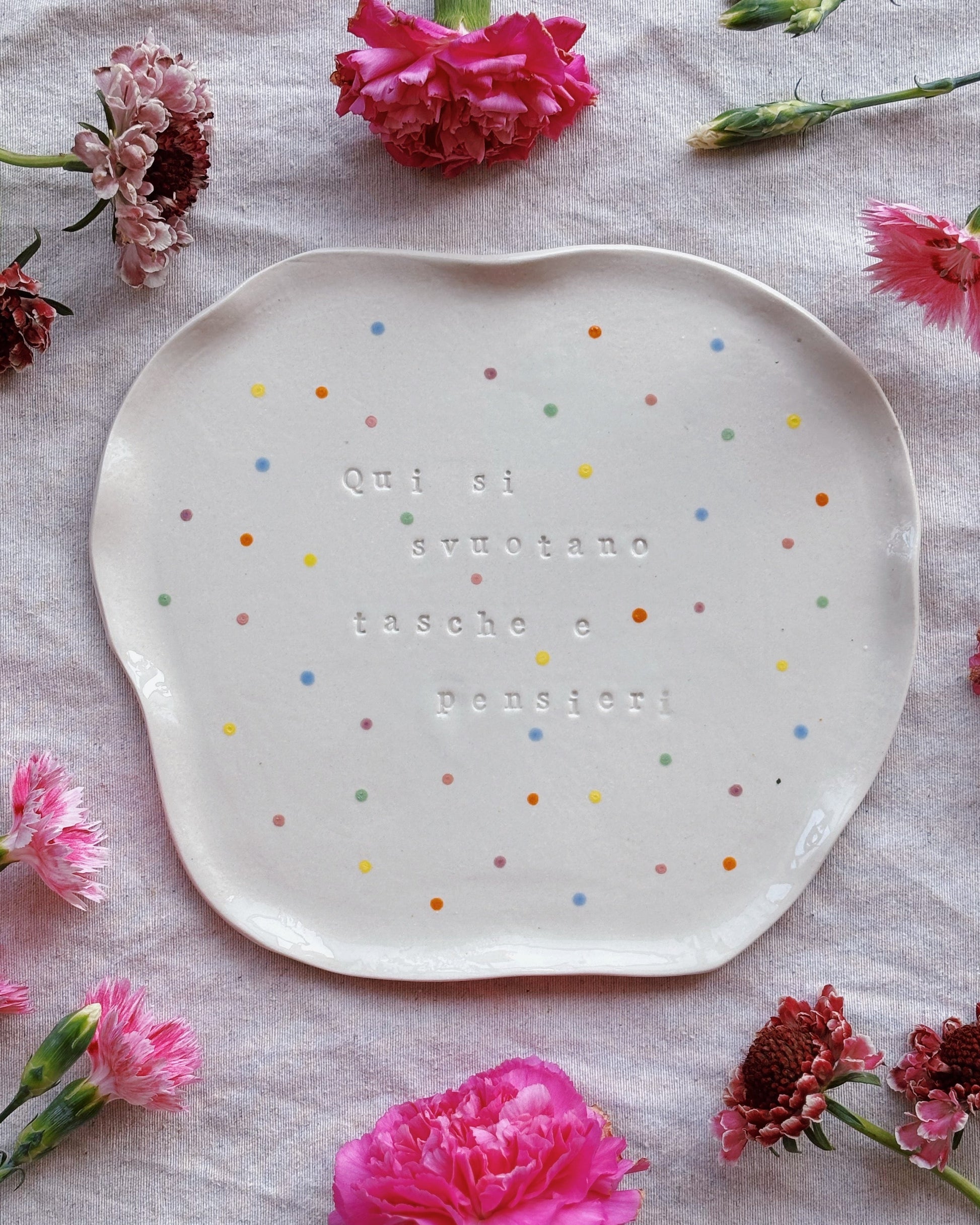 Decorative plate with colorful polka dots and text on a tablecloth with pink flowers.