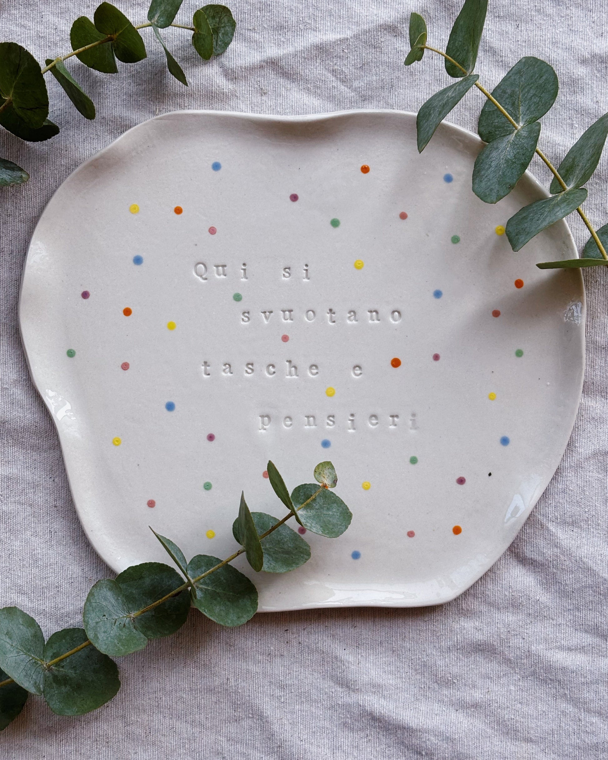 Polka dot ceramic plate with text on a gray surface with eucalyptus leaves.
