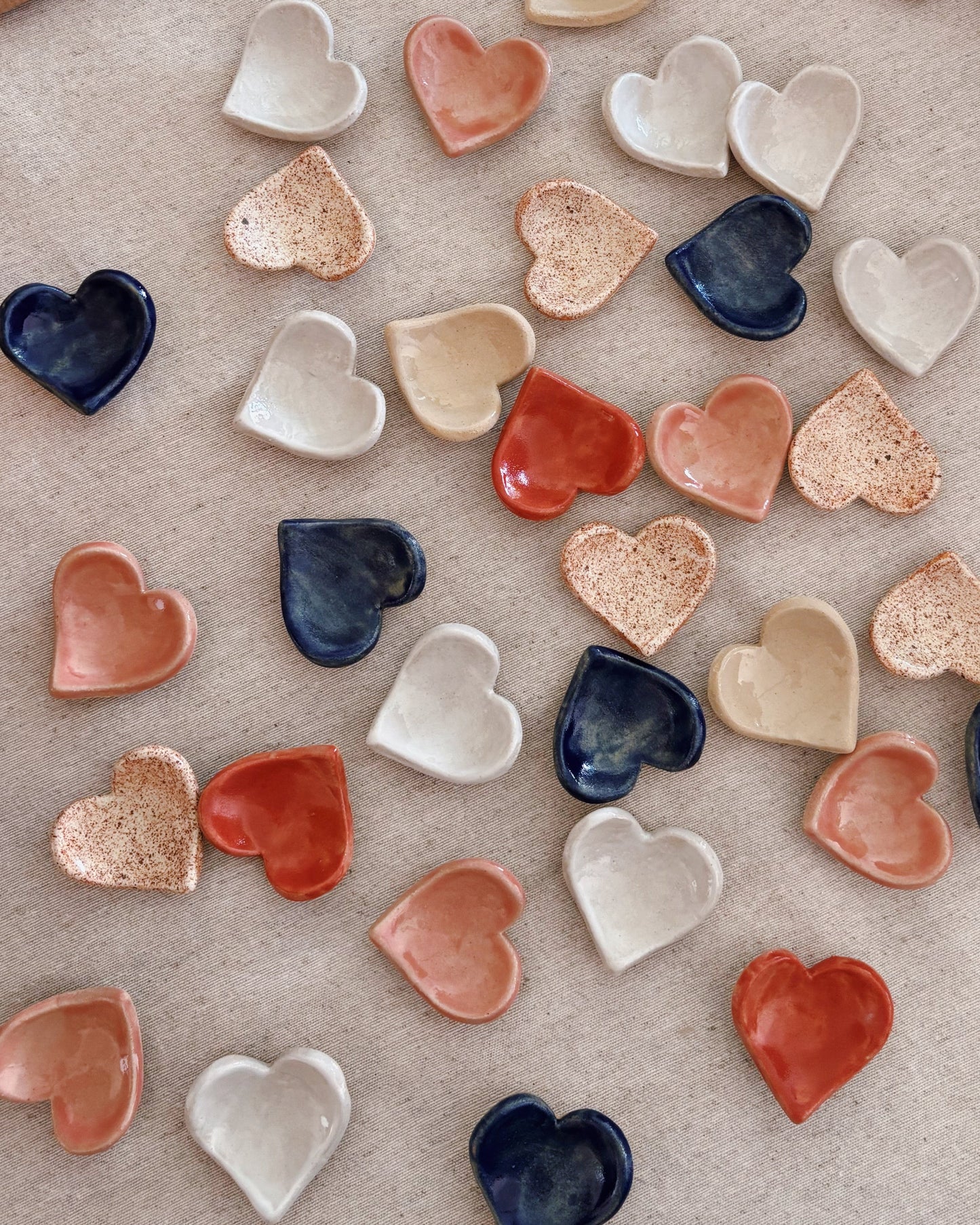 Colorful heart-shaped ceramic pieces on a textured surface with brown paper packages.