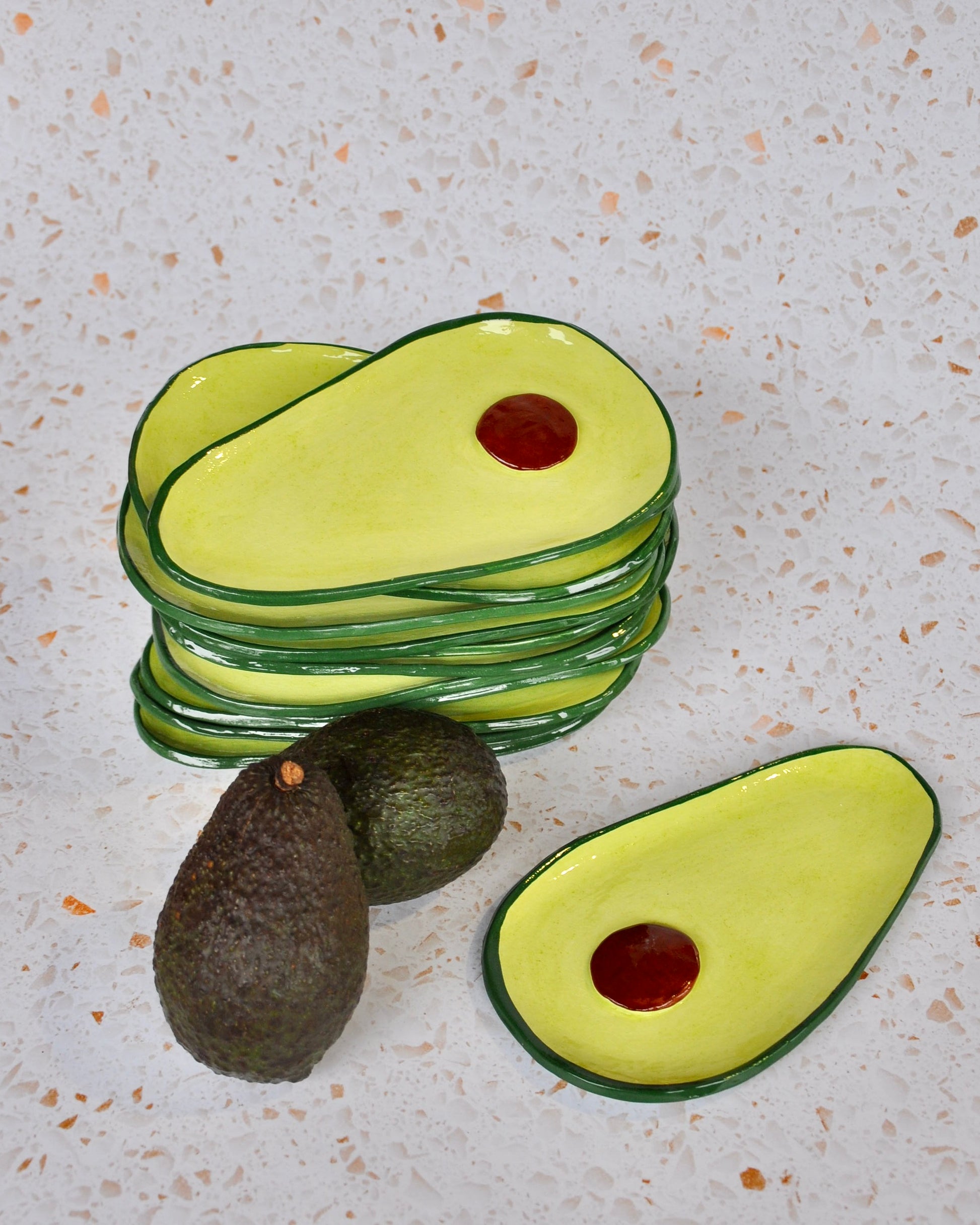 Avocado Spoon Rest set stacked on a countertop with whole avocados beside them.