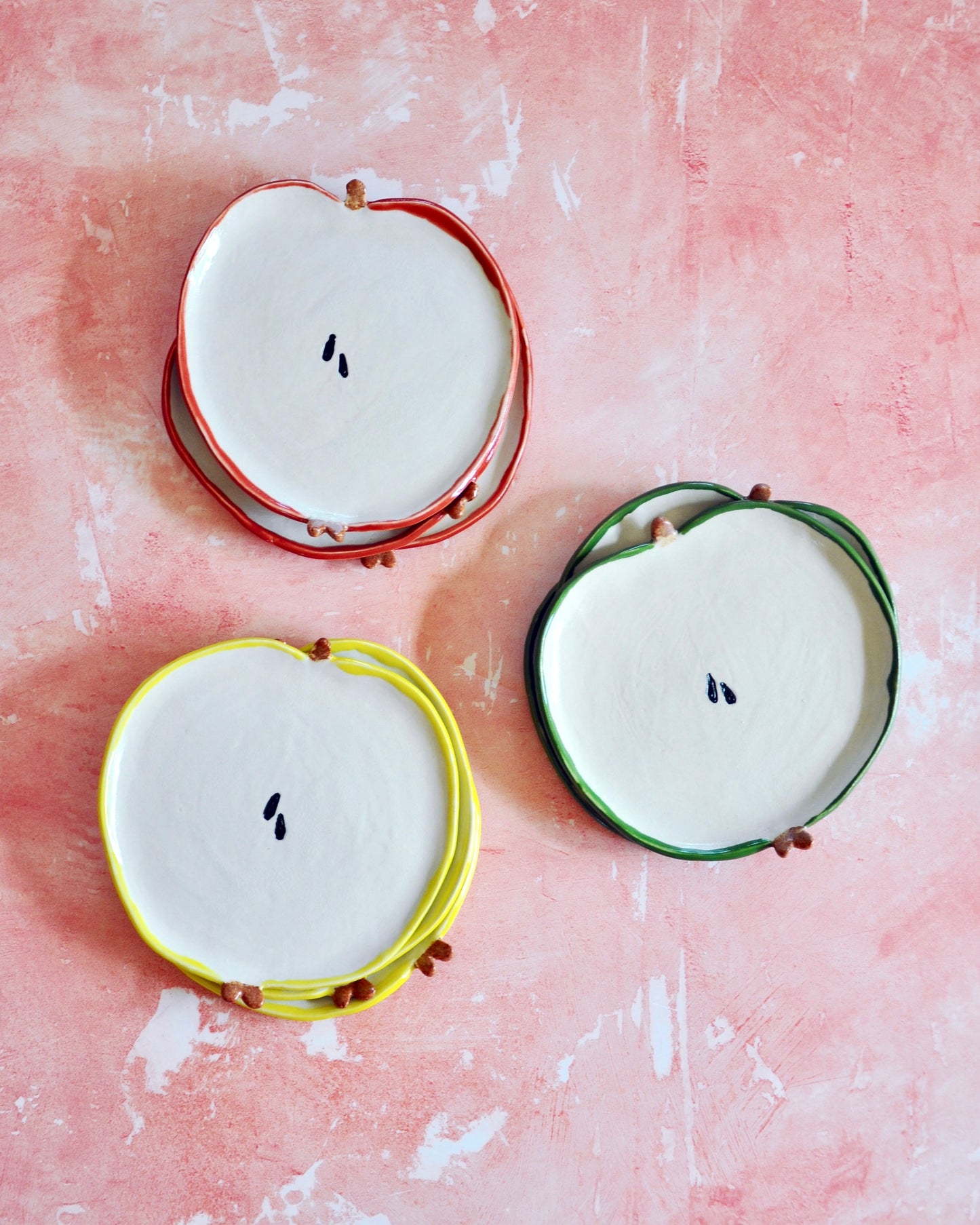 Colorful Apple Spoon Rest set on a pink background, handmade stoneware ideal for kitchen use.