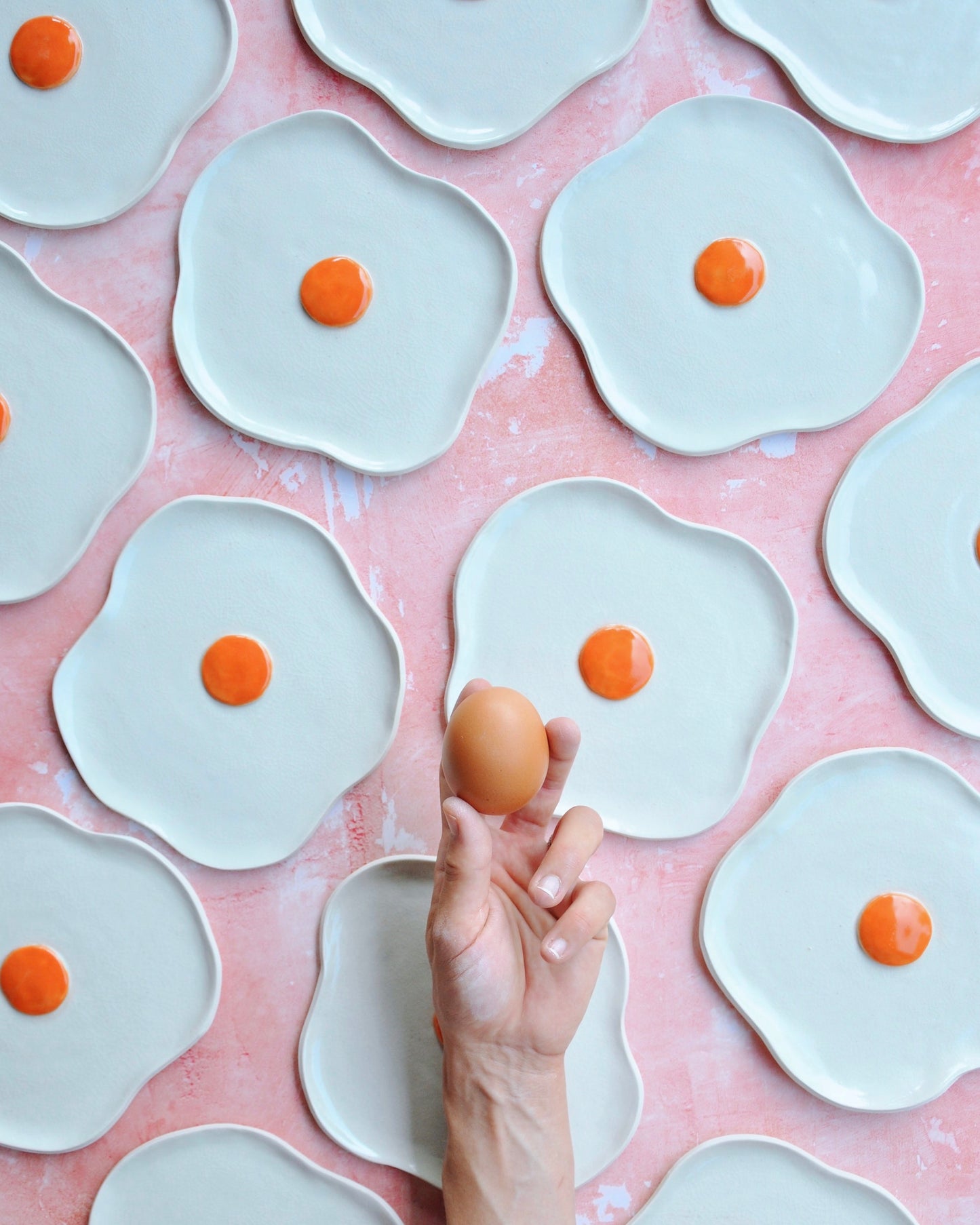 Egg Spoon Rest made of stoneware with an egg being held over decorative plates in a fun kitchen setup.