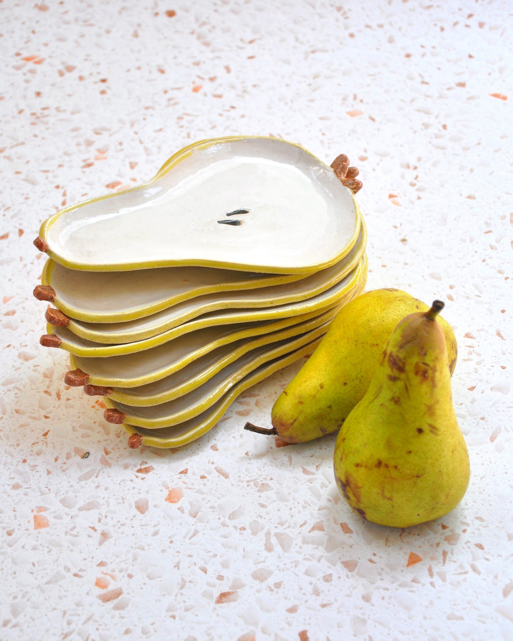 Set of Pear Spoon Rests stacked beside fresh pears, showcasing handmade stoneware, ideal for kitchen decor.