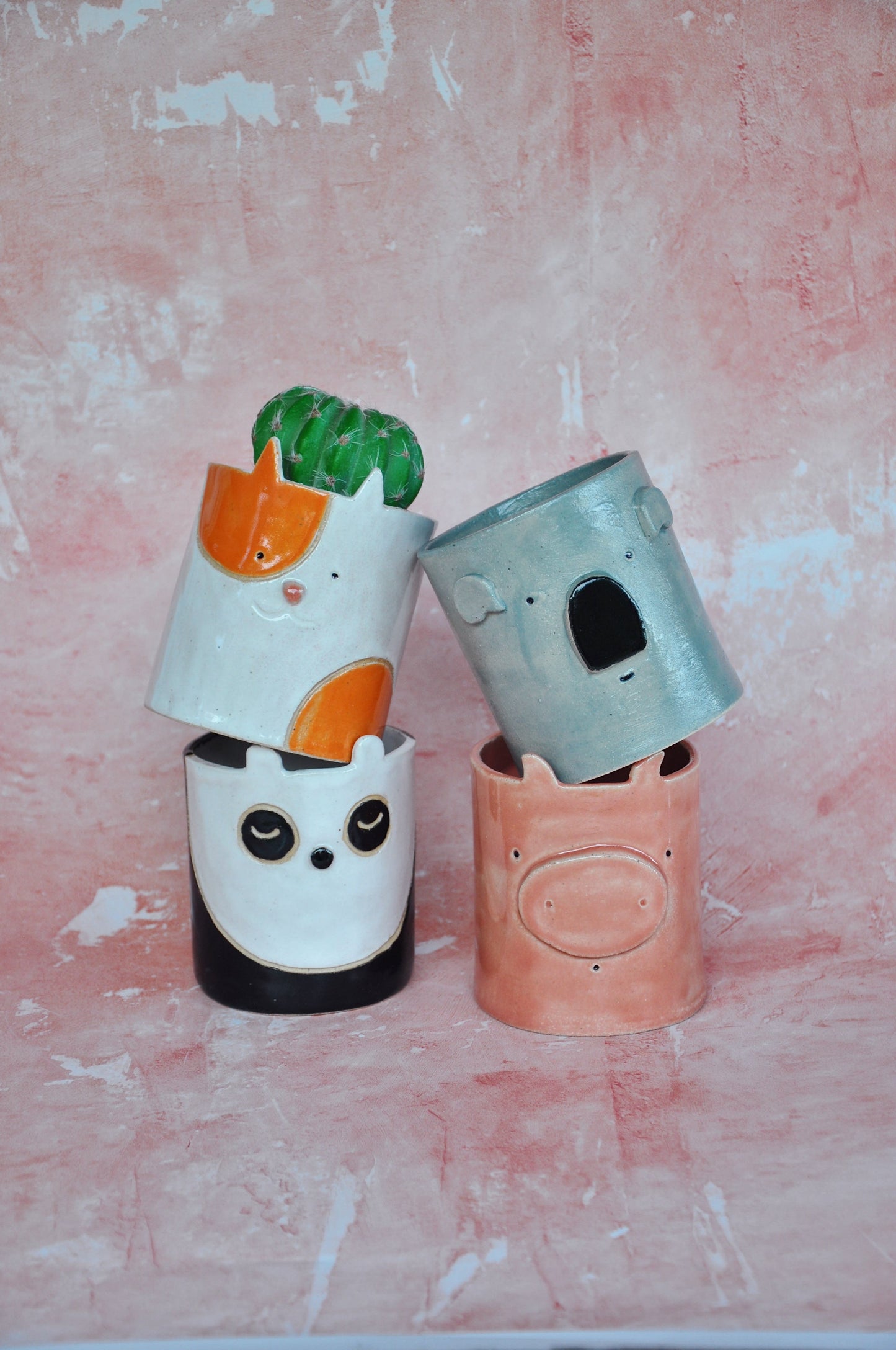 Four handmade decorative planters stacked, featuring animal designs and a vibrant color palette.