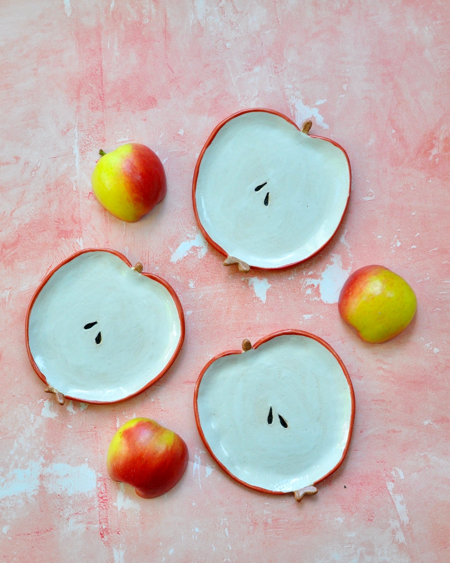 Handmade Apple Spoon Rest on a pink background with small apples beside it, ideal for kitchen décor.